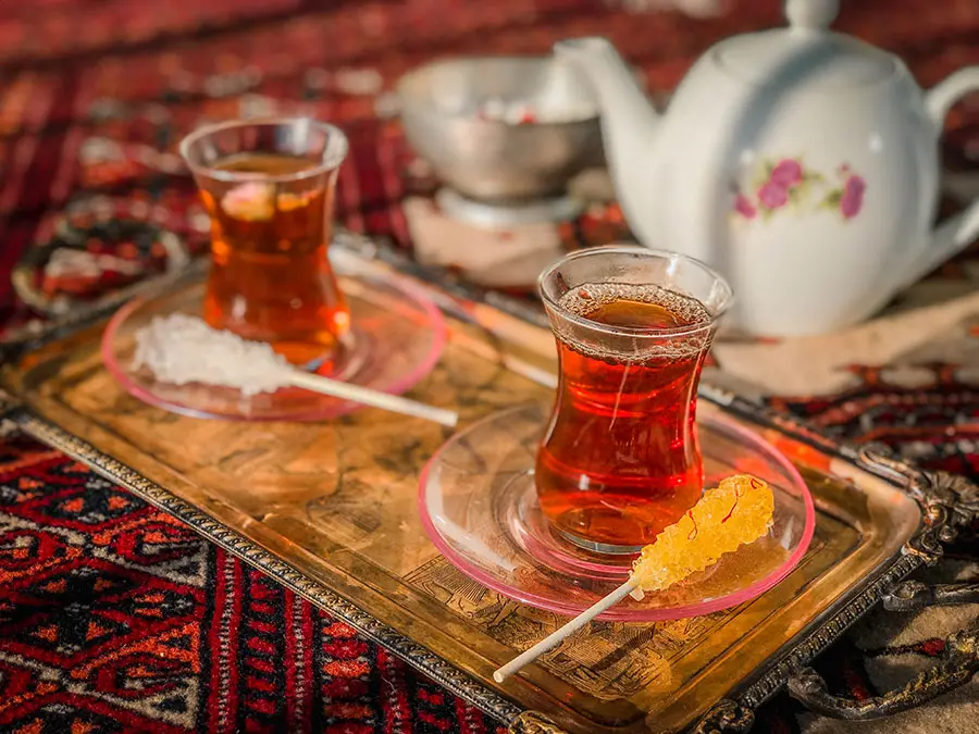 چای ایرانی سنتی در فنجان سفالی با برگ‌های تازه و ادویه